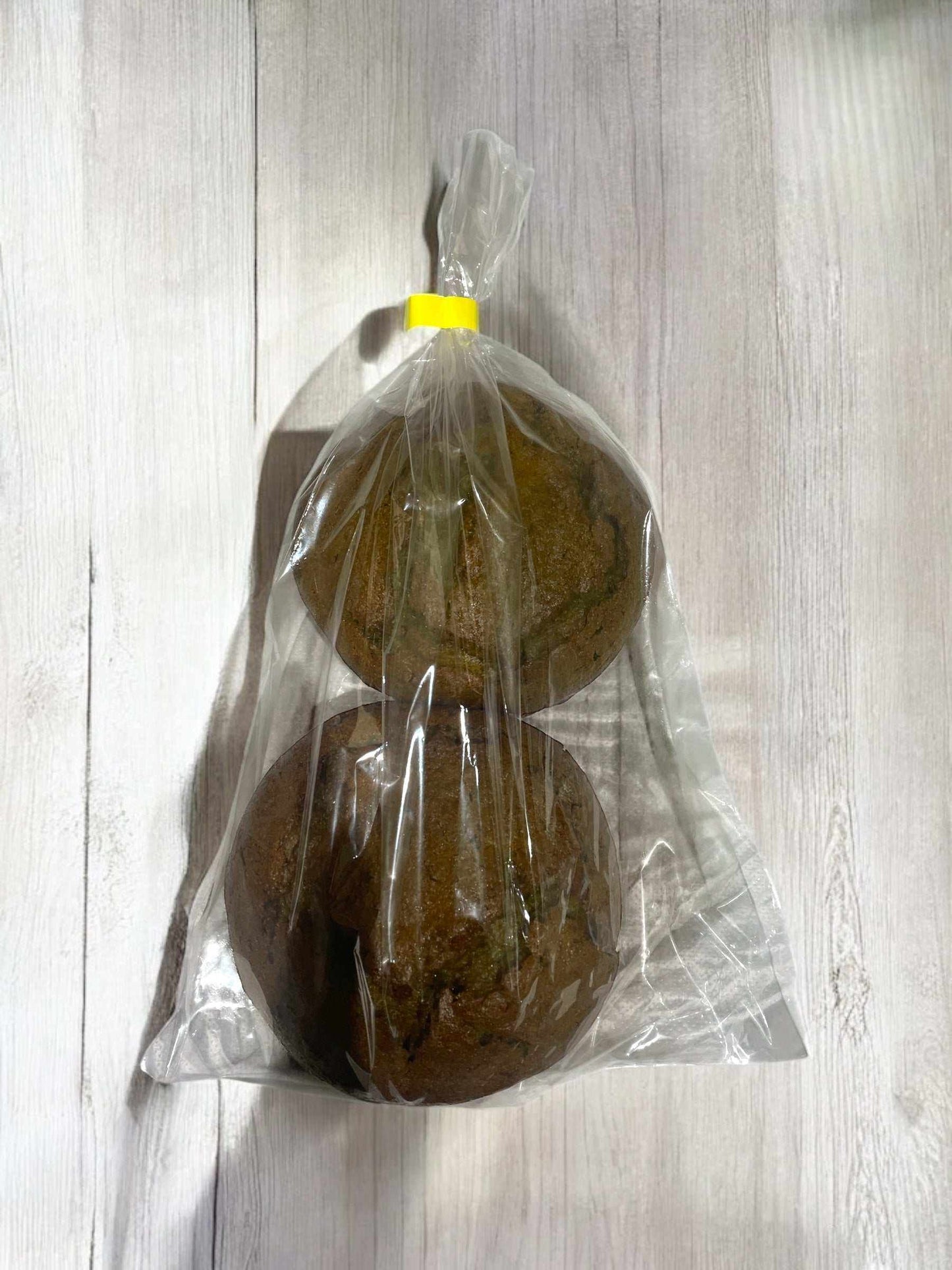 Two classic matcha muffins in clear plastic bag with yellow tie on light wooden surface