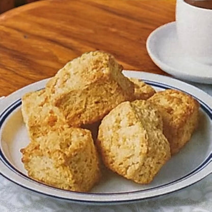 Plate of six plain scones with a golden crust on a wooden table next to a white cup