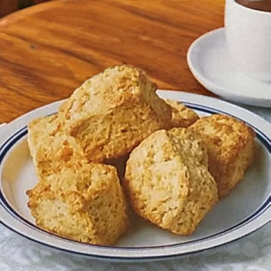 Plate of six plain scones with a golden crust on a wooden table next to a white cup